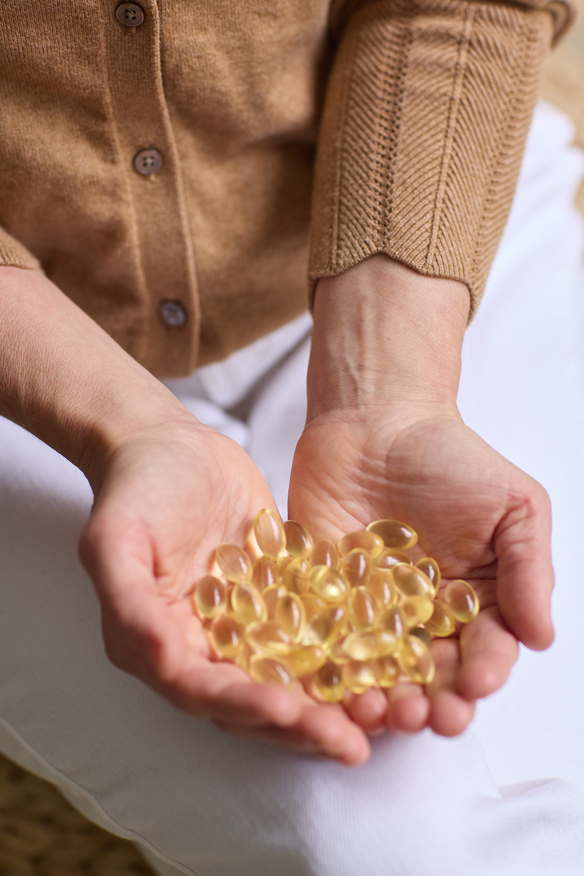 A white woman in a brown cardigan and white jeans holding 60 days worth of the best fish free algae omega 3 pregnancy capsules in her hards.